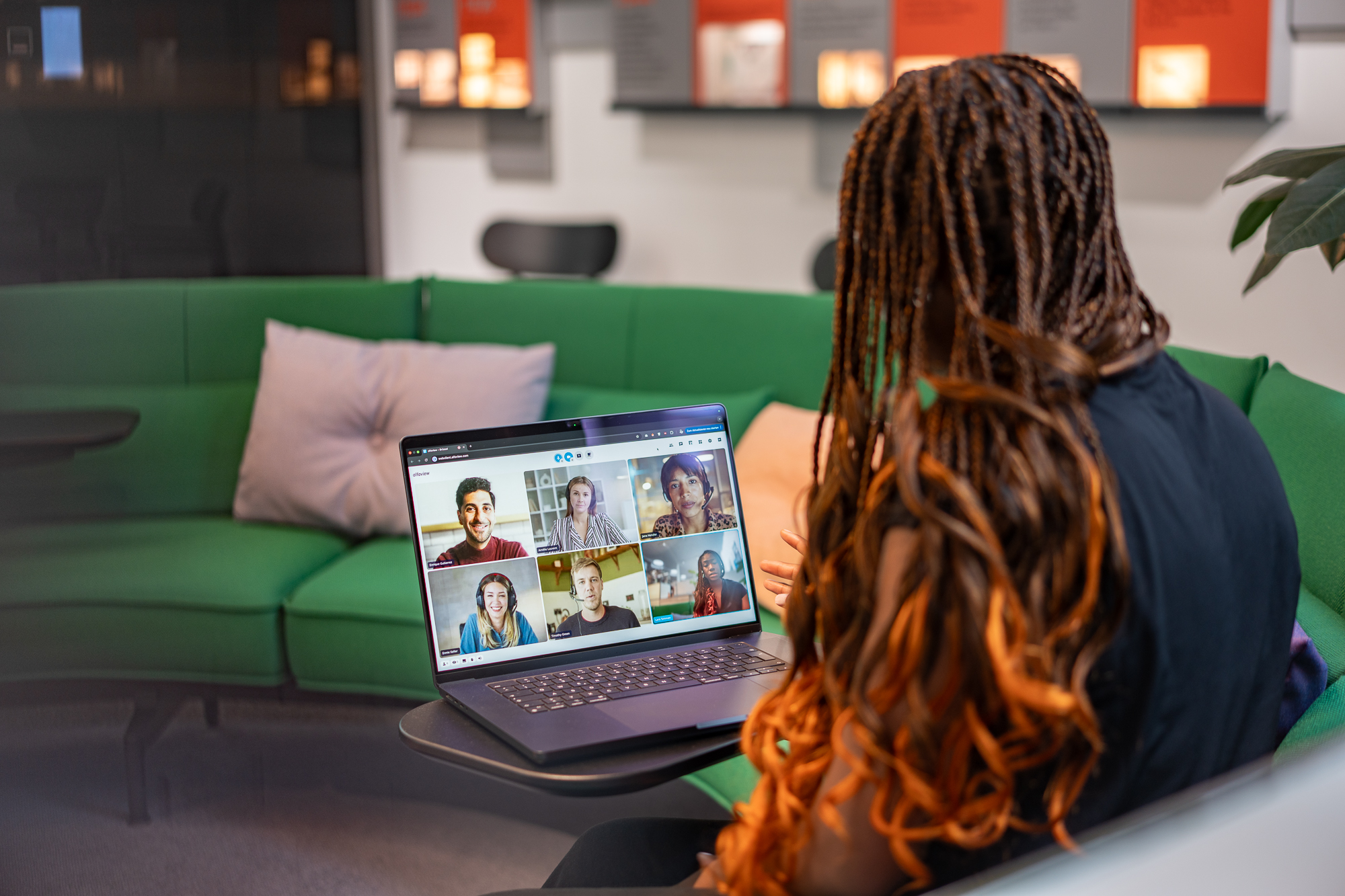 Frau sitzt auf Sofa und nimmt mit Laptop an Videokonferenz teil.